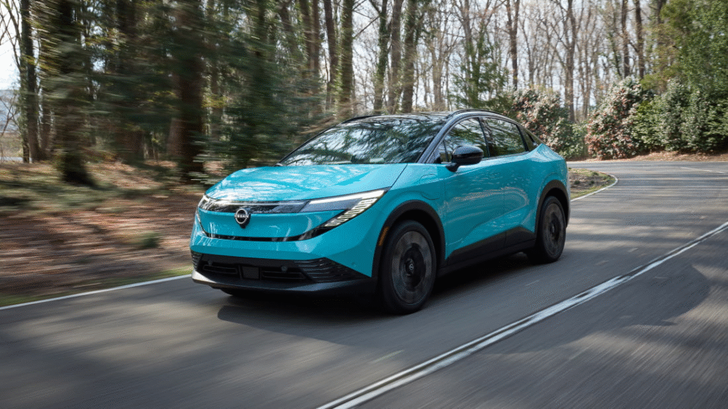 2026 Nissan Leaf electric crossover driving on forest road, showcasing sleek aerodynamic design in blue