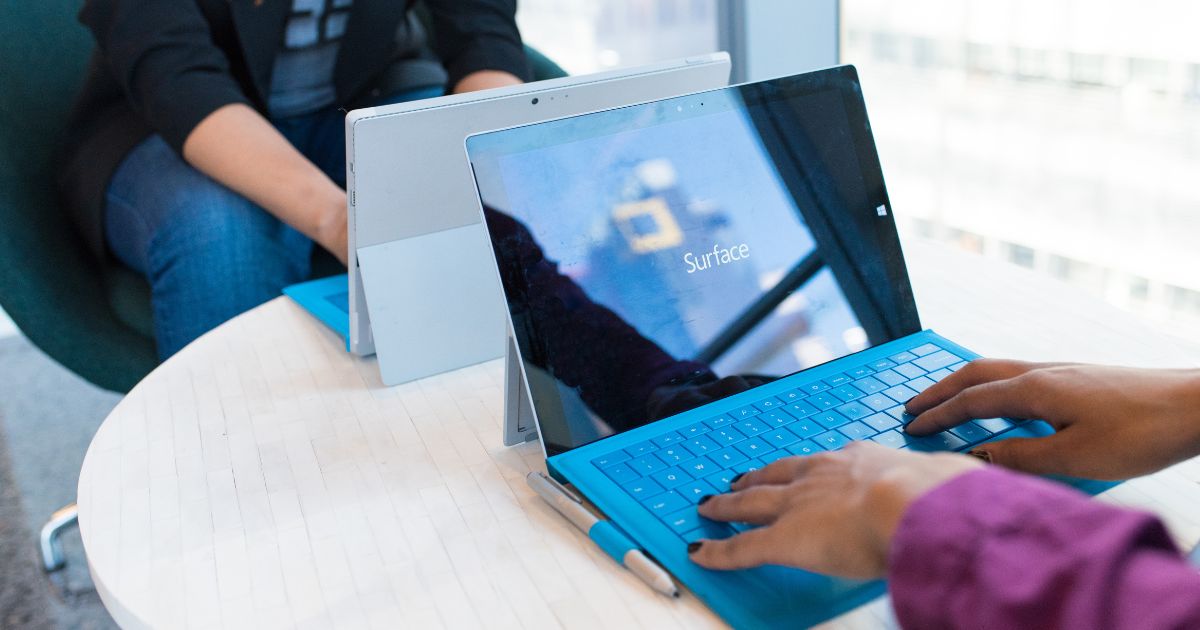 Two people using Microsoft Surface laptops at a modern workspace, showcasing Windows 11 interface updates – thinknfree.com