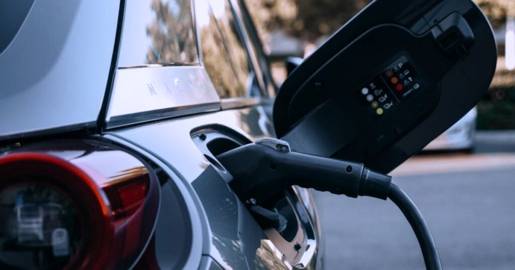A close-up shot of a black electric vehicle charging cable plugged into the open charge port of a modern, dark-gray ev car