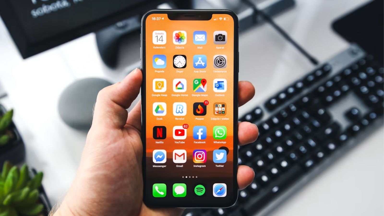 Hand holding an iPhone showing its Home Screen with app icons